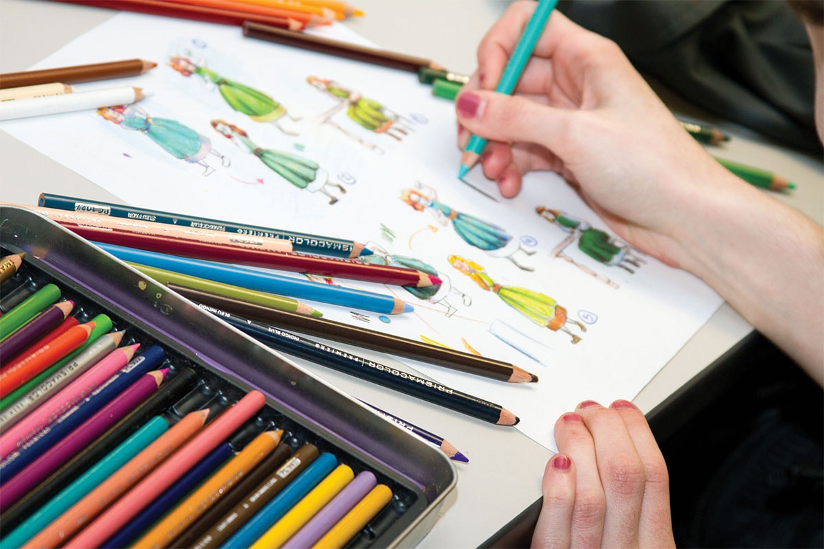 Primer plano de una alumna de DigiPen dibujando un personaje con lápices de colores al lado.