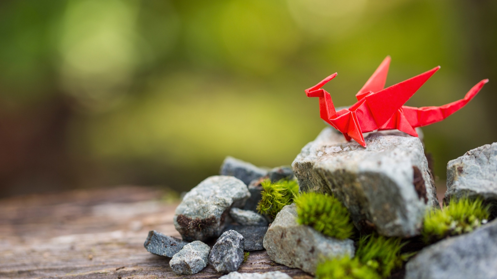 Un dragón de papel origami rojo sobre una roca cubierta de musgo.