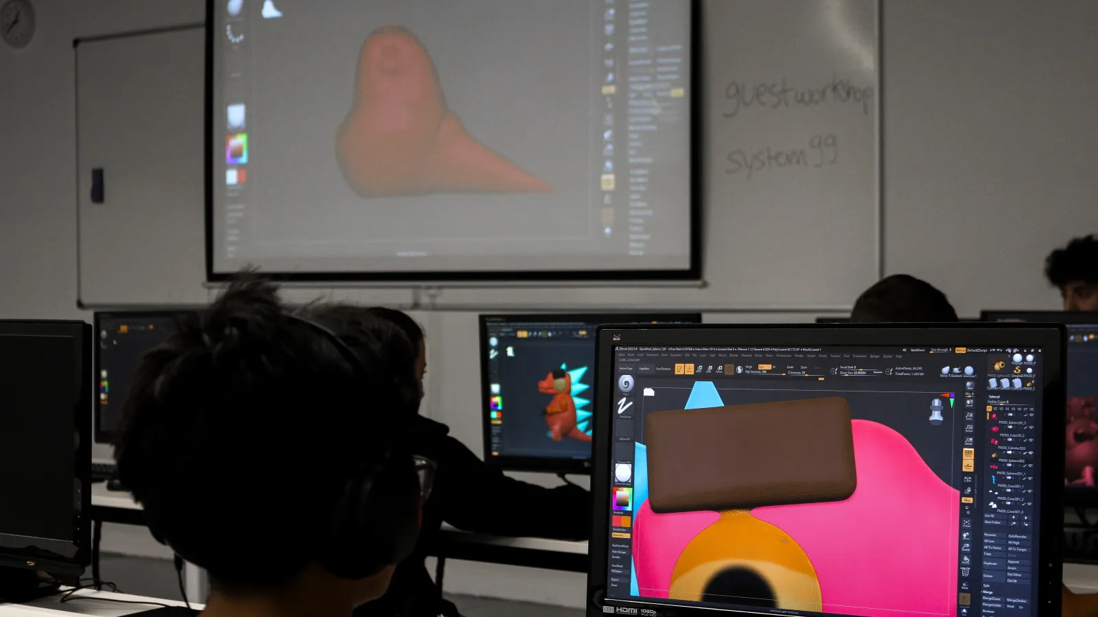 Un estudiante parece enfocado en los detalles de su proyecto mientras una referencia se muestra en el monitor