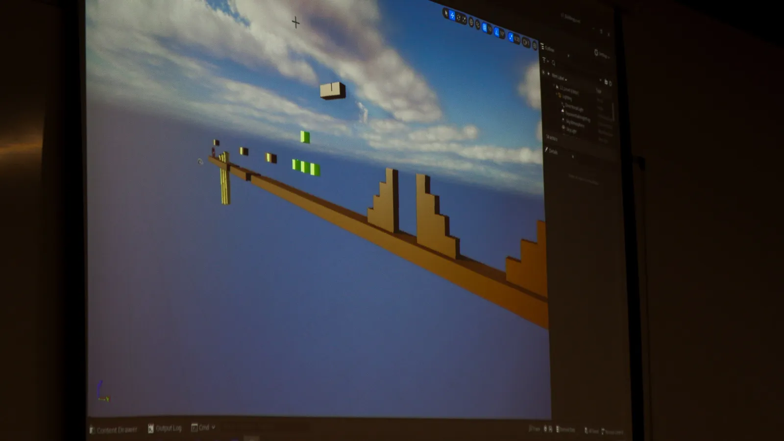 Big screen shows the example used by the instructor on how to create a simple game environment, with different obstacles and platforms, in the Unreal Engine editor