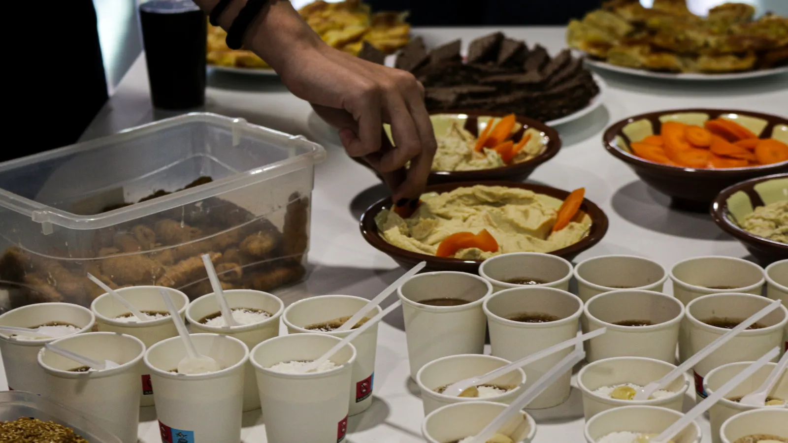 Hummus y diferentes alimentos de distintas naciones, distribuidos en vasos para autoservicio.