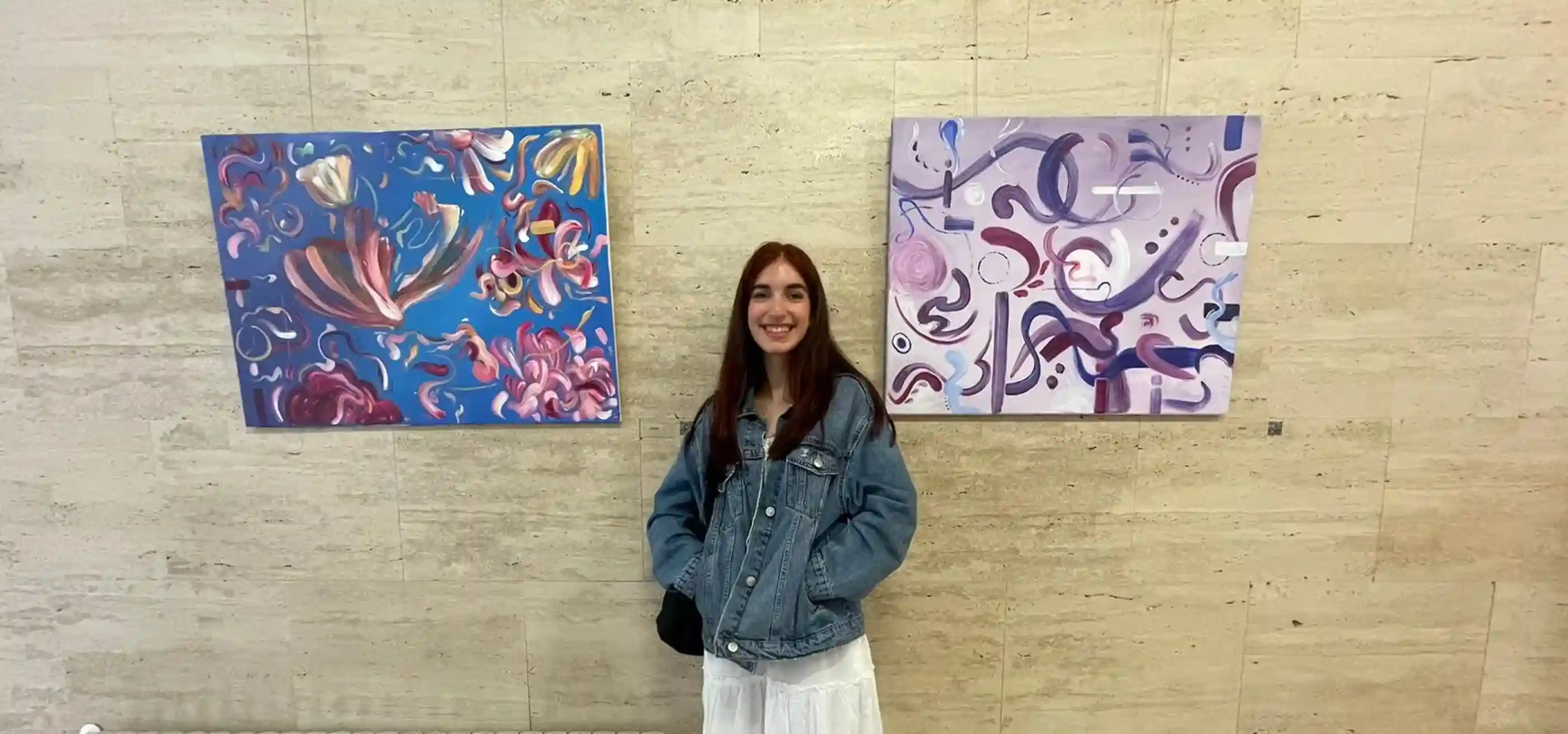 Nerea Ayala Castellanos standing between two abstract paintings on a stone wall.