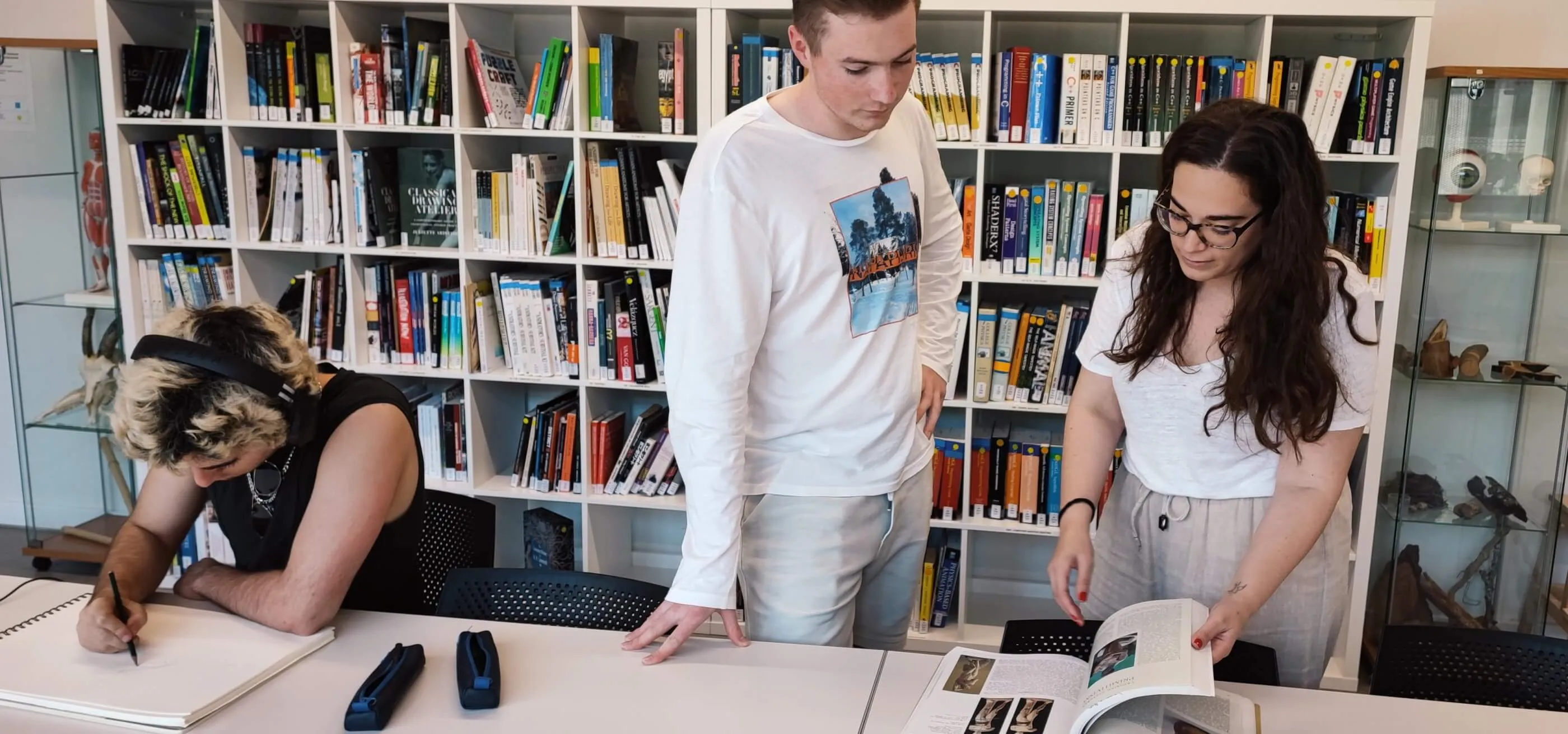 Un estudiante y la bibliotecaria ojean un libro en de la biblioteca de DigiPen Europe-Bilbao