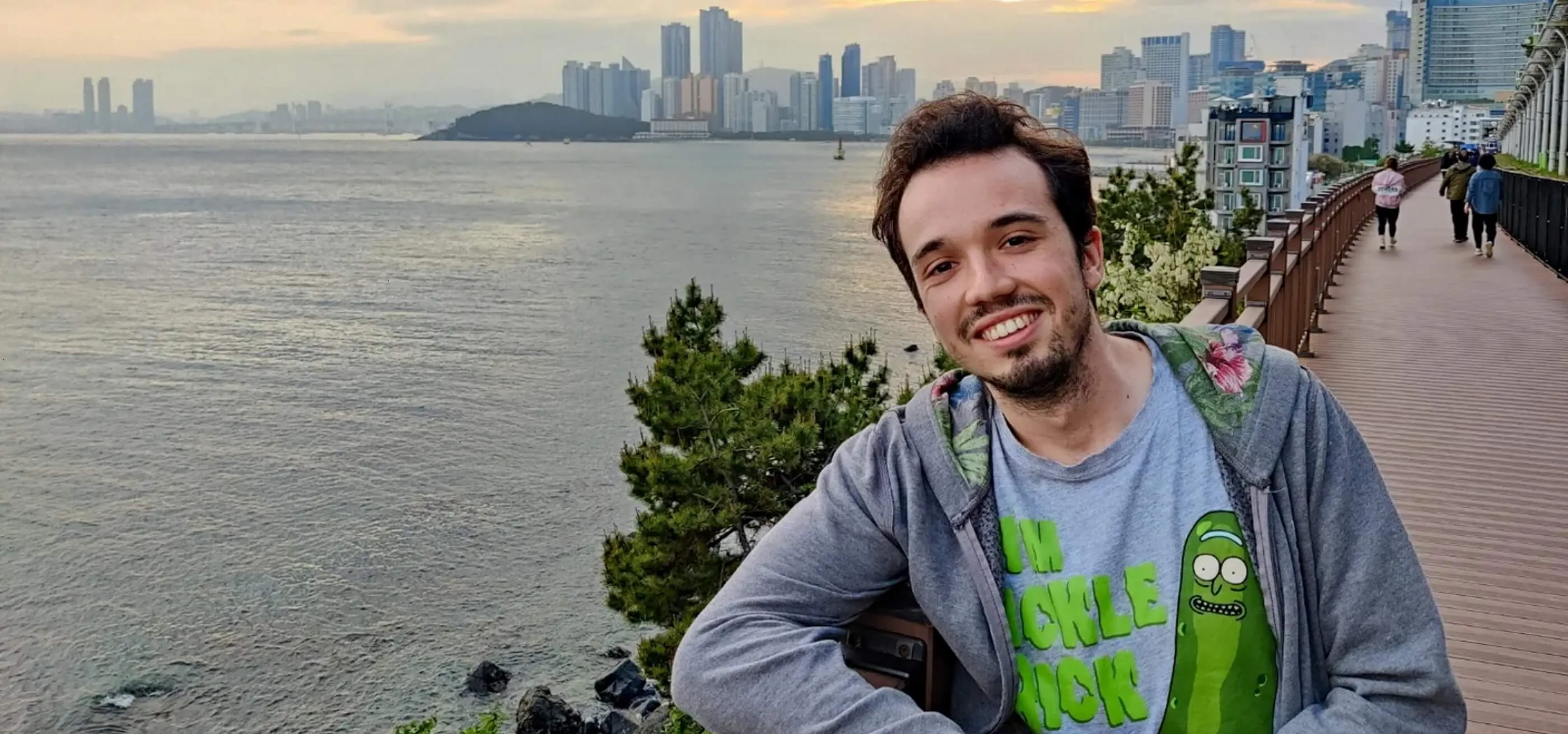 DigiPen alumnus Jon Zapata leans against a railing set against a city skyline next to water