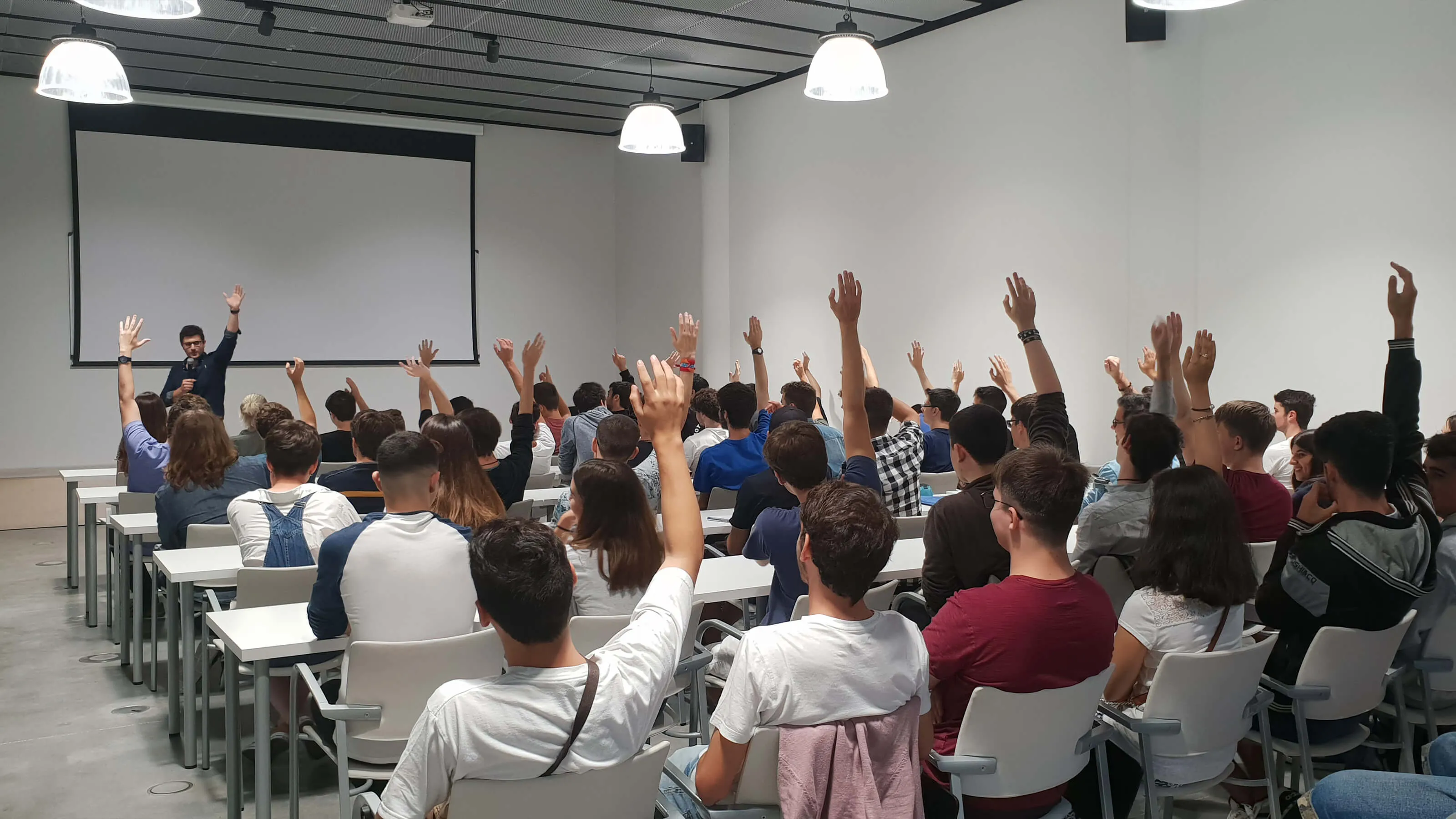 An instructor stands before a group of seated students with their hands raised