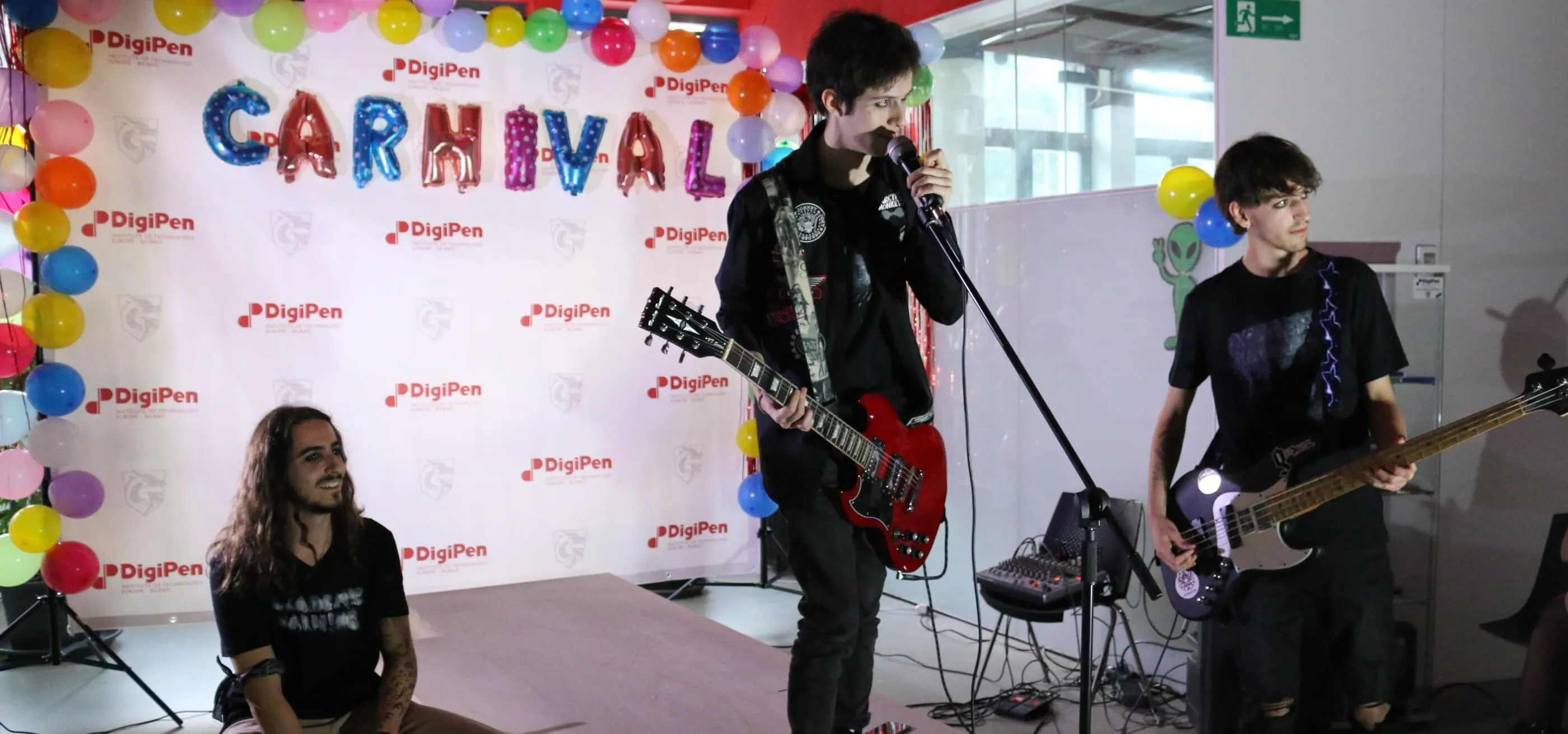 Three student band members perform on a stage with the word &#039;Carnival&#039; behind them