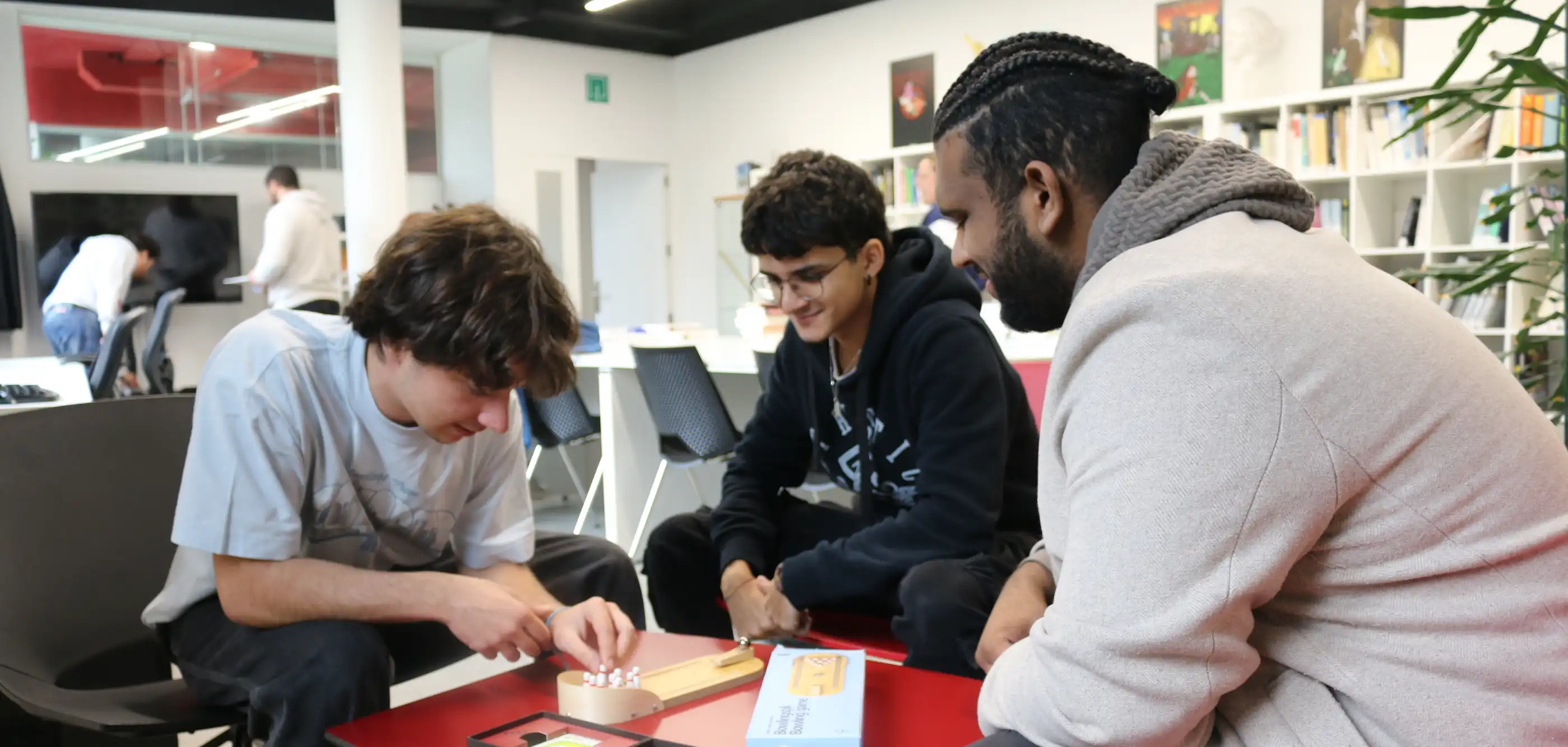 Estudiantes jugando a un juego de mesa en grupo, sentados alrededor de una mesa en la biblioteca de DigiPen Europe-Bilbao.