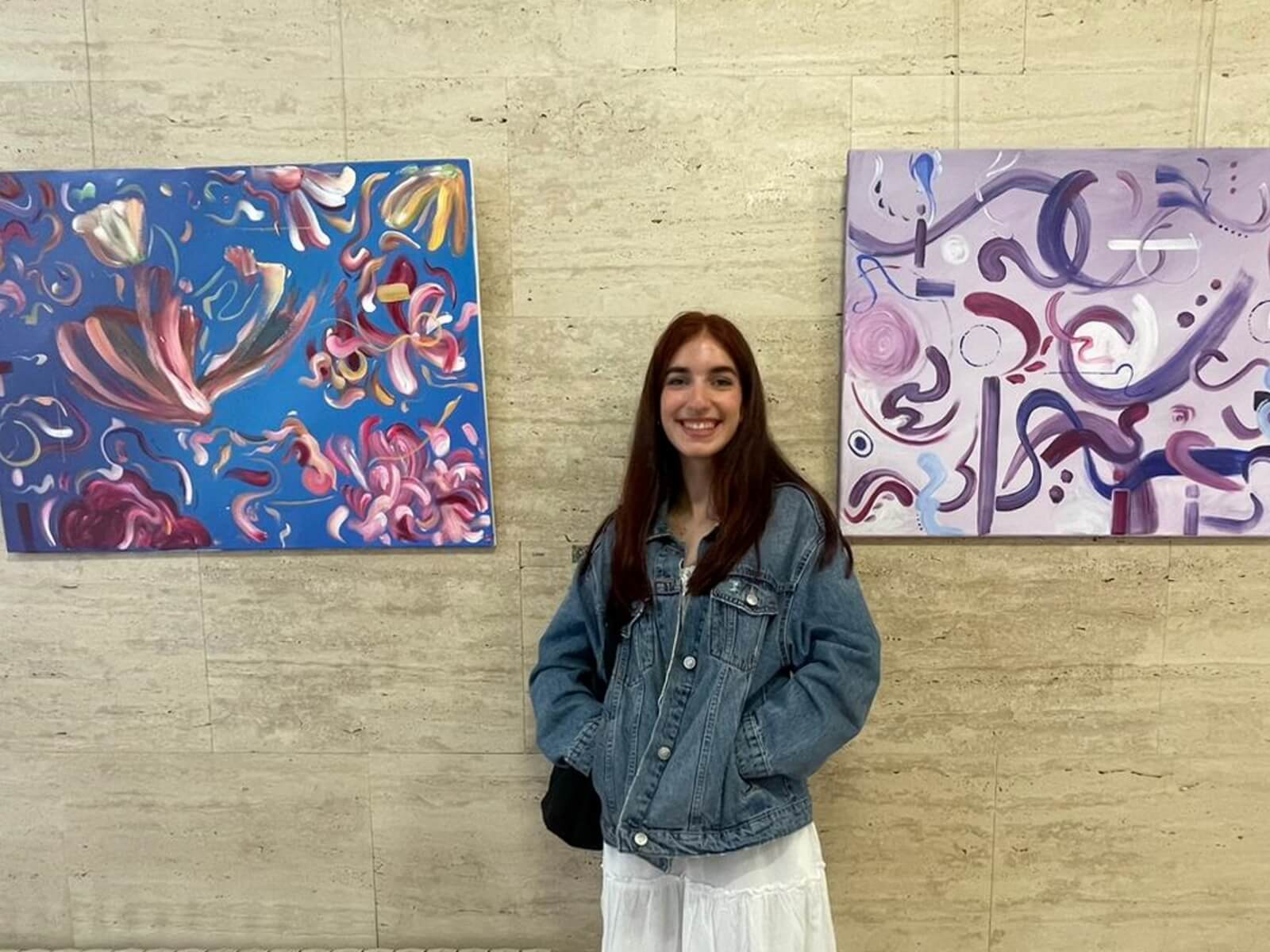 Nerea Ayala Castellanos standing between two abstract paintings on a stone wall.
