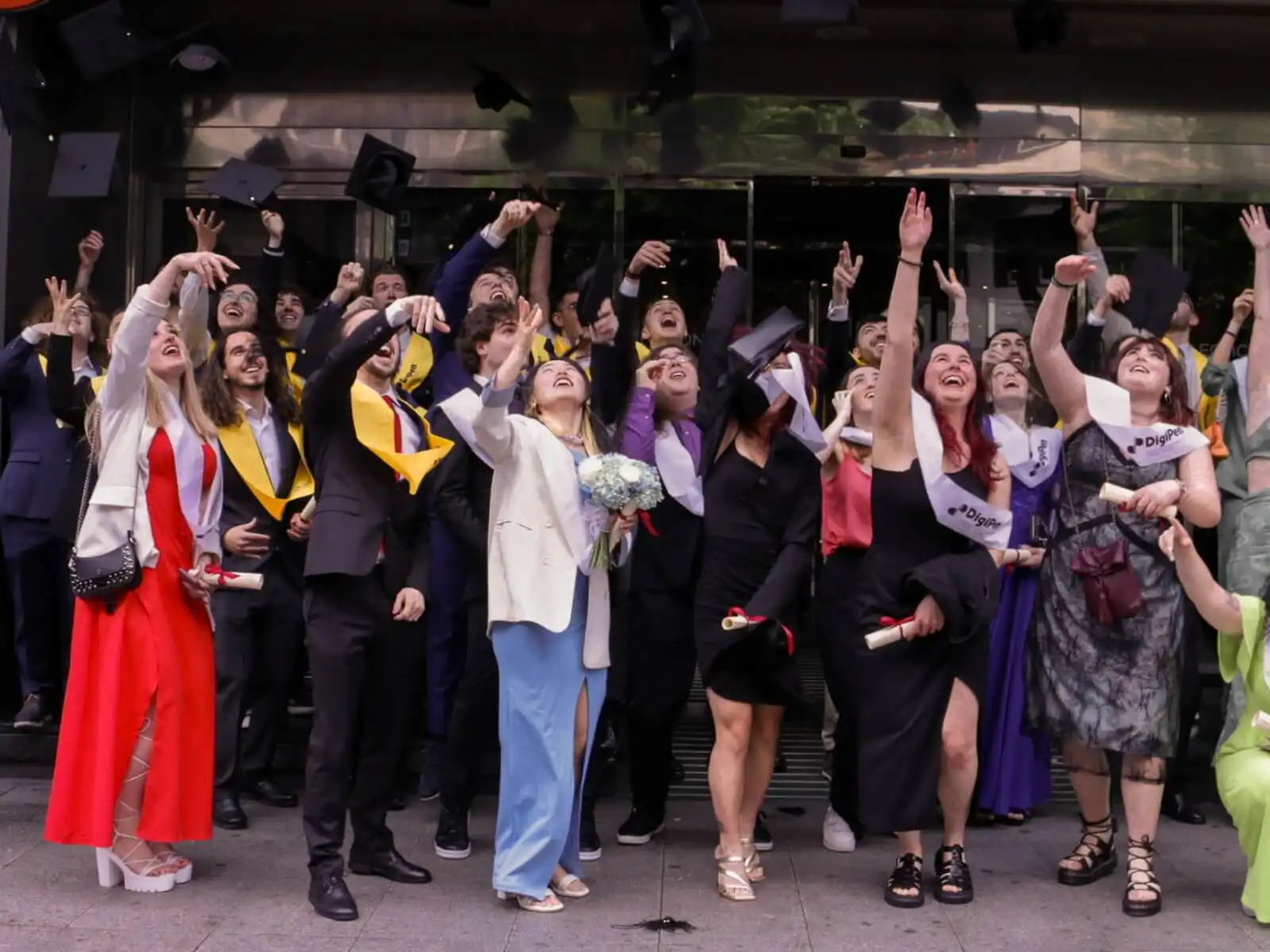 Los graduados de DigiPen Europe-Bilbao, vestidos con togas y birretes, lanzan alegremente sus birretes al aire mientras están de pie afuera de un edificio