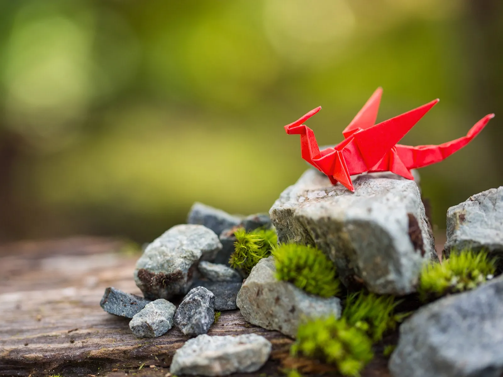 A dragon crafted from red origami paper sitting on a mossy rock.