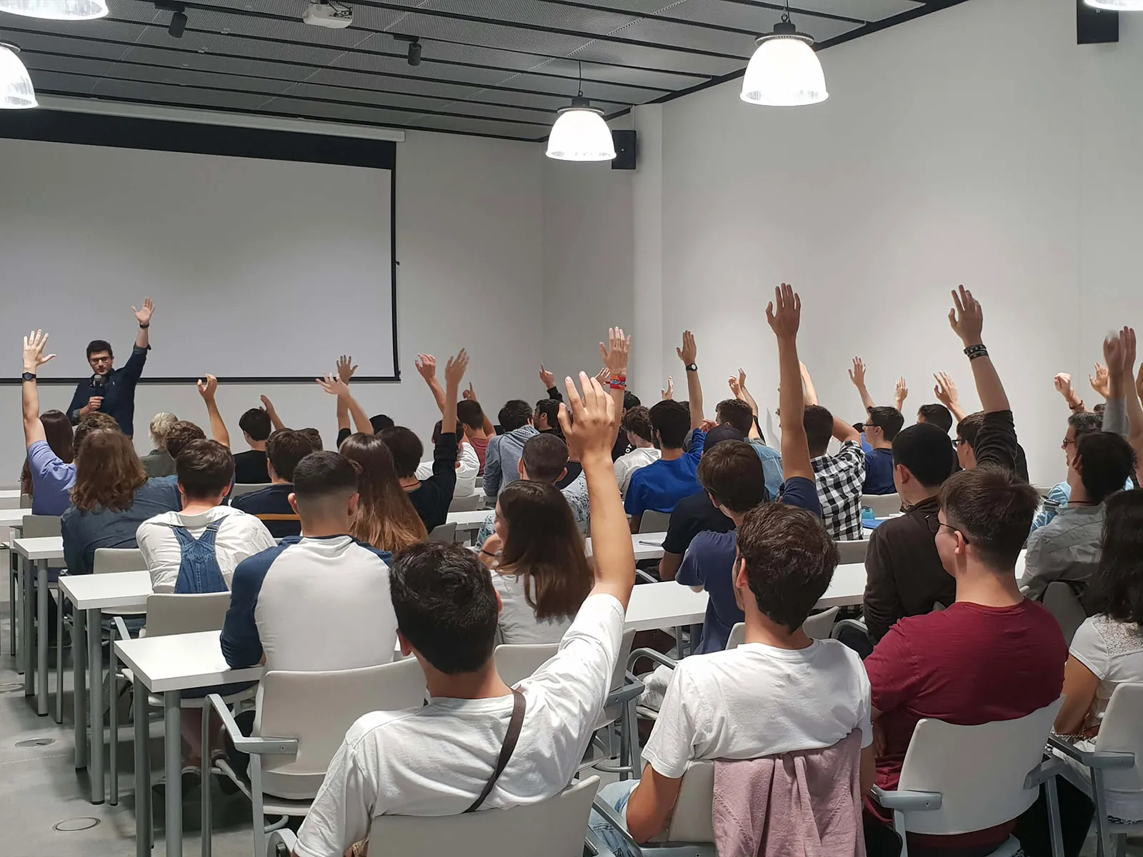 An instructor stands before a group of seated students with their hands raised