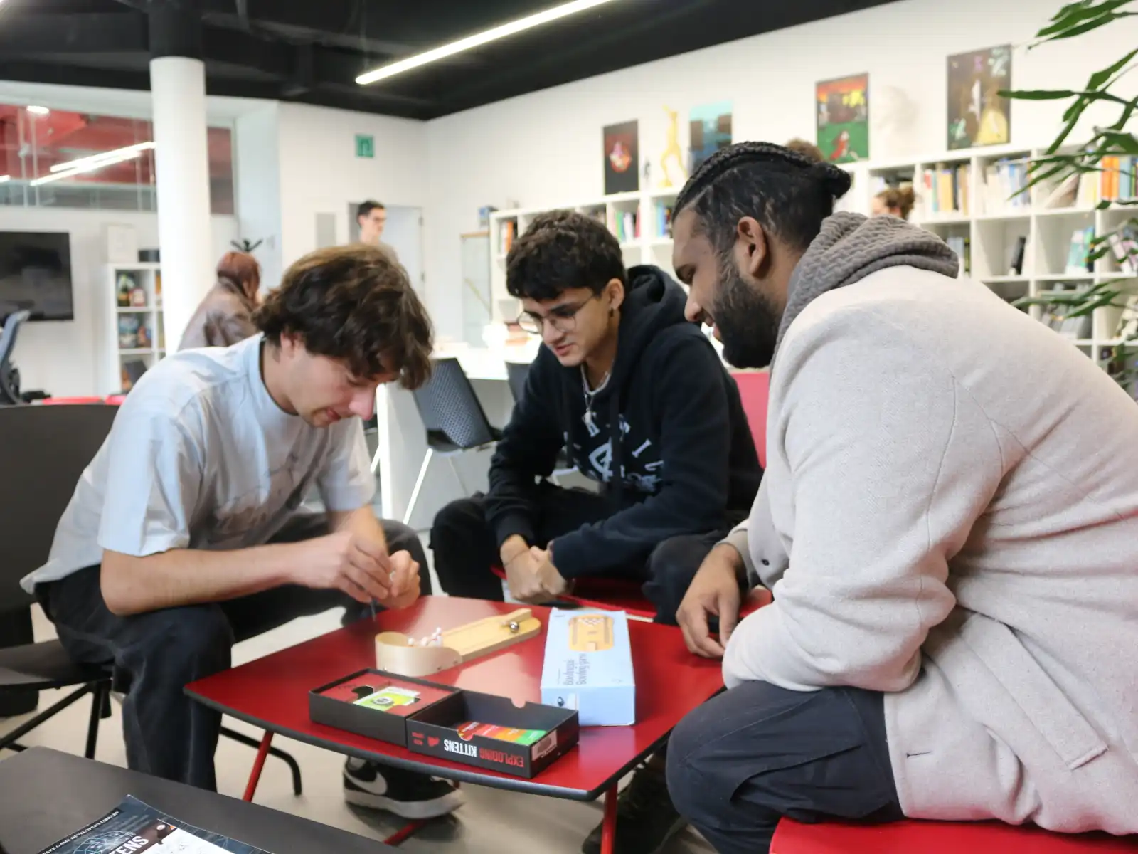 Students playing a board game as a group, sitting around a table in the library at DigiPen Europe-Bilbao.