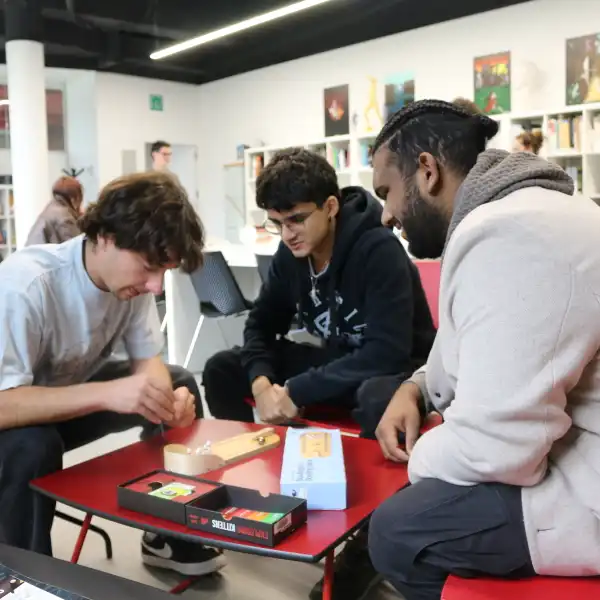 Estudiantes jugando a un juego de mesa en grupo, sentados alrededor de una mesa en la biblioteca de DigiPen Europe-Bilbao.