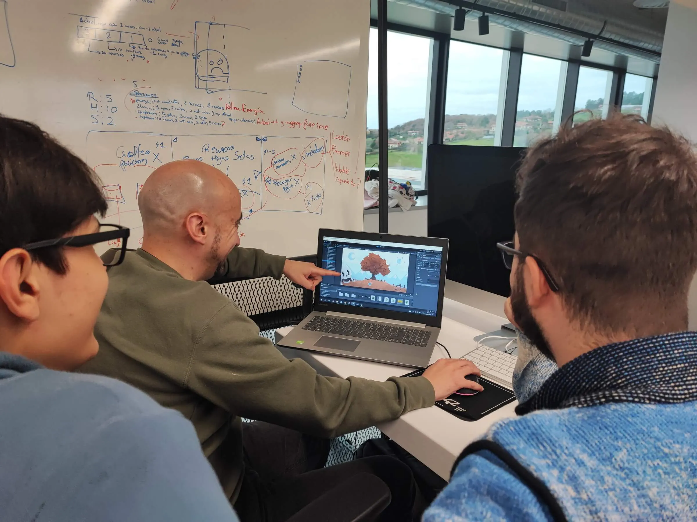 Three students sit around a laptop and look at a game being developed in the Unity game engine.