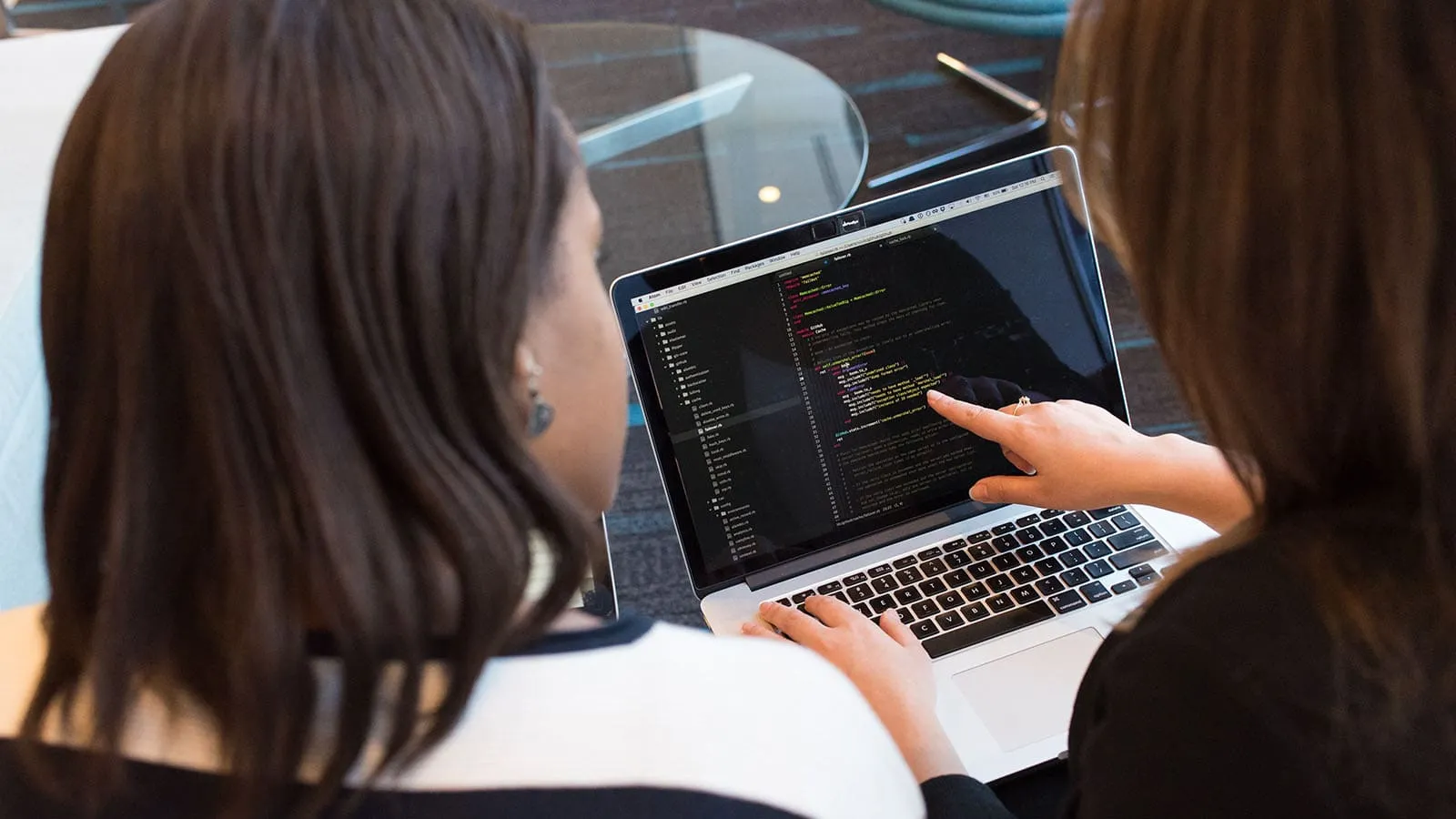 Two girls read code in an editor and learn programming while interacting in front of a laptop.