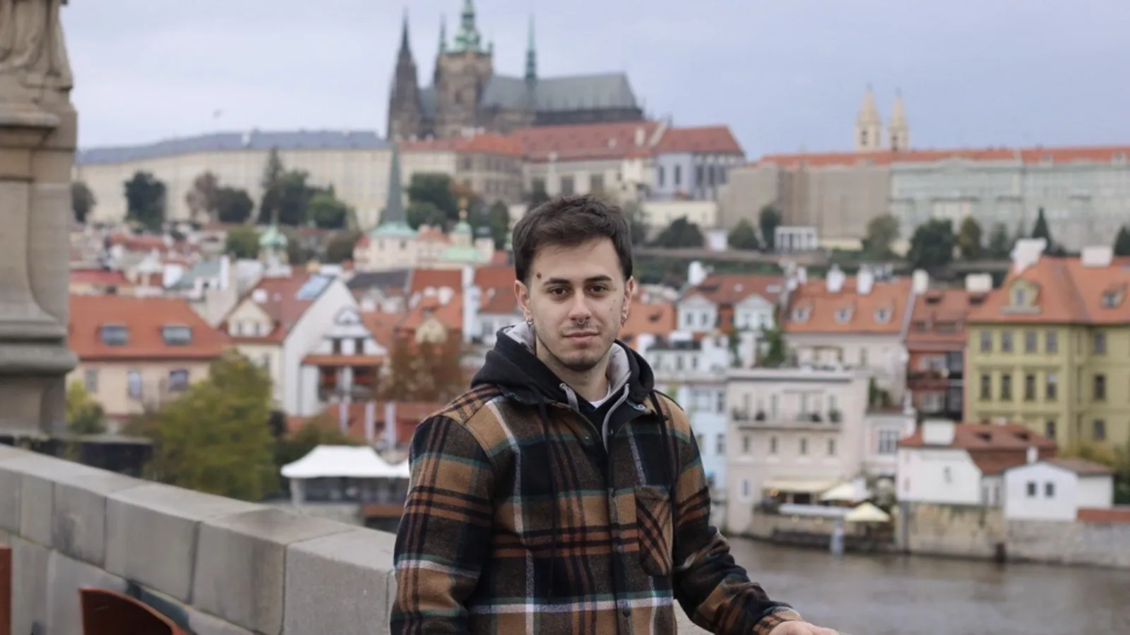 Portrait of Jonathan Cáceres standing on a bridge with a scenic cityscape of Prague in the background.