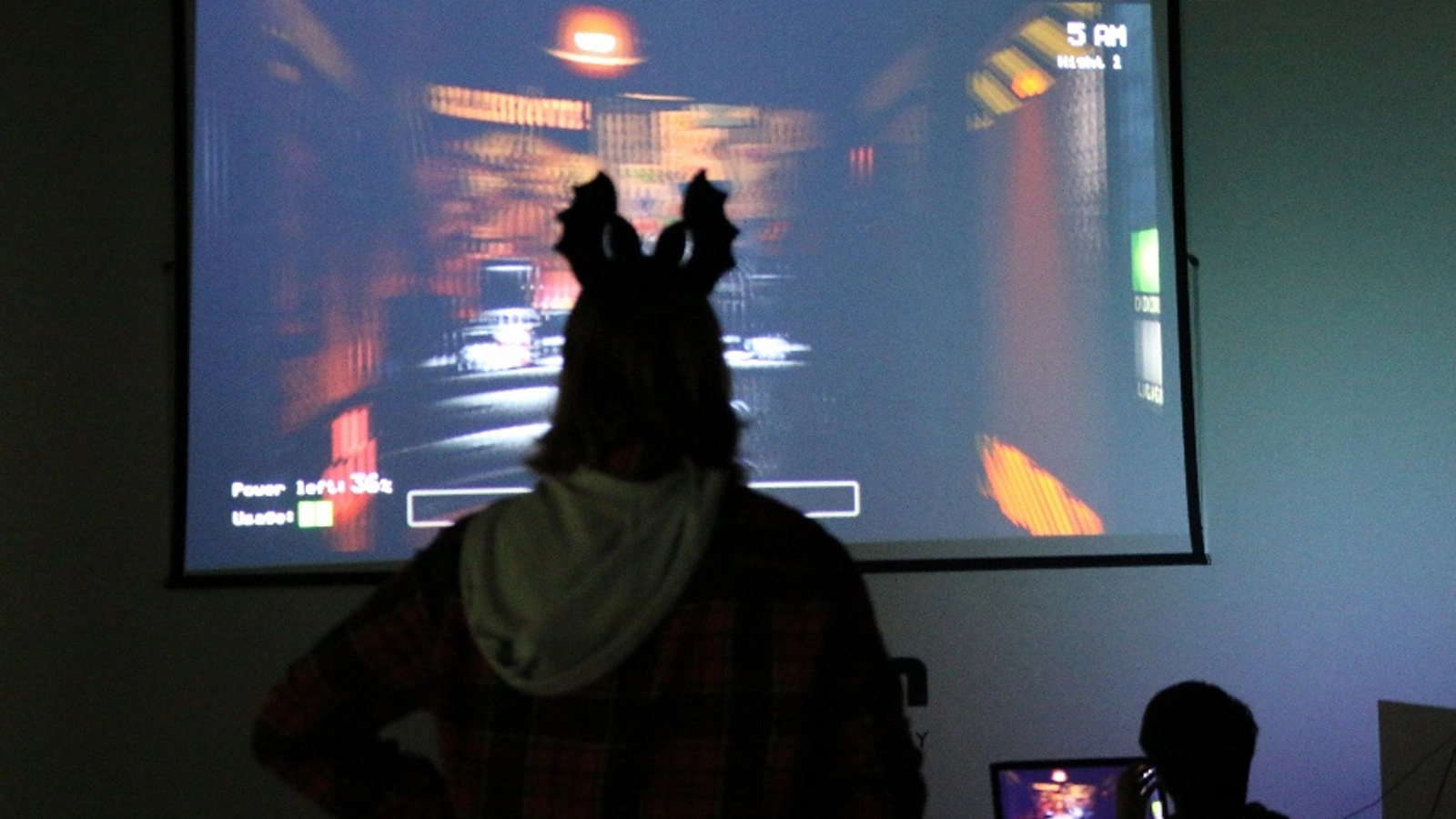 Students at DigiPen playing horror games during Halloweek’s Horror Game Night. A student with Halloween antlers watches the screen intently.