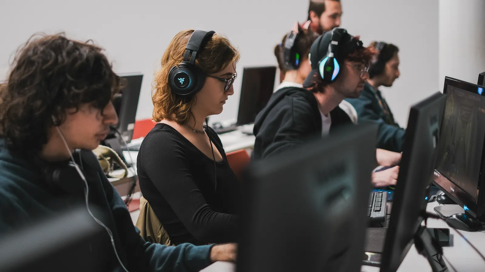 Students at DigiPen Europe-Bilbao focused on their computer screens, playing Valorant during a tournament, with gaming headsets on.