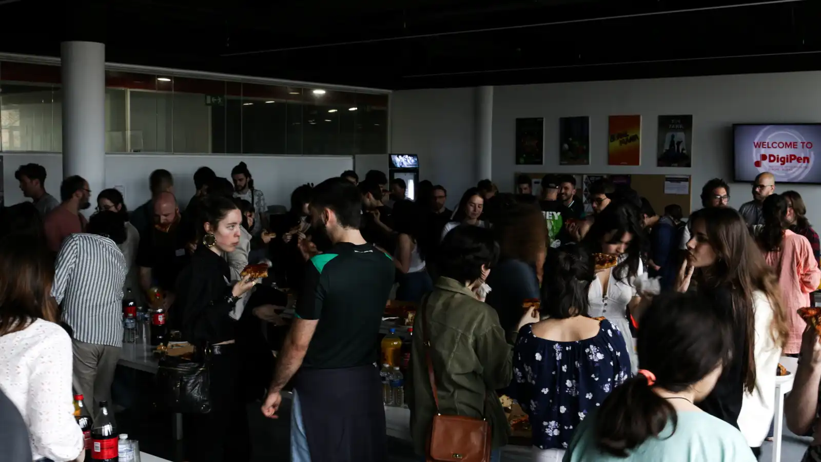 Alumnis, profesorado y administracion socializan durante una reunión con pizza y refrescos.