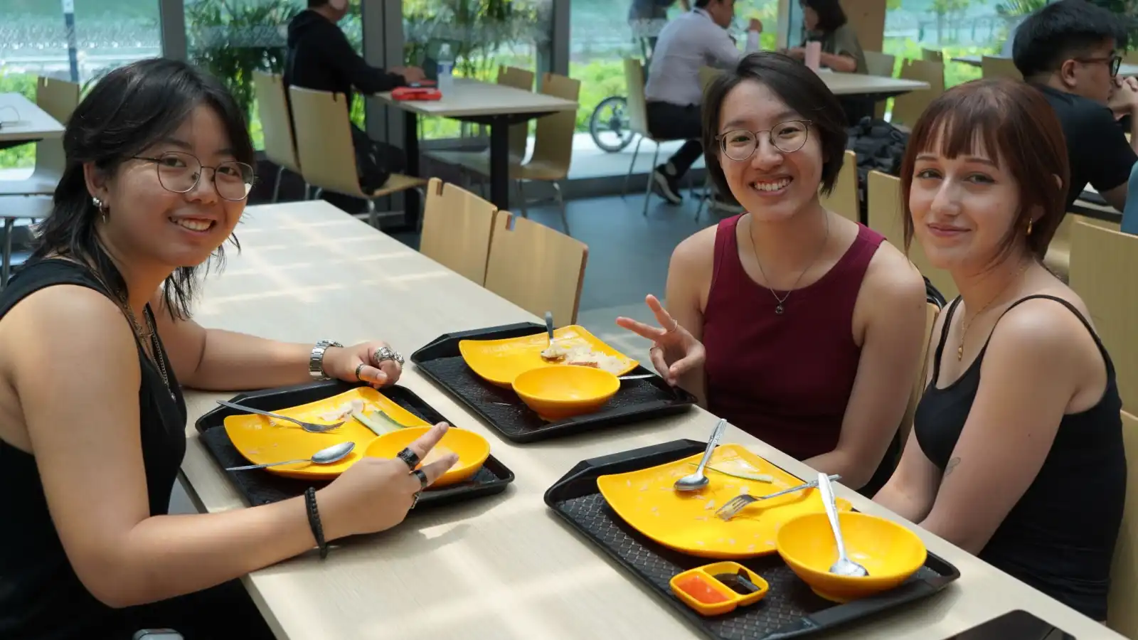 Alumnado de DigiPen Singapur y Bilbao disfrutando de una comida juntas en un comedor moderno y luminoso.