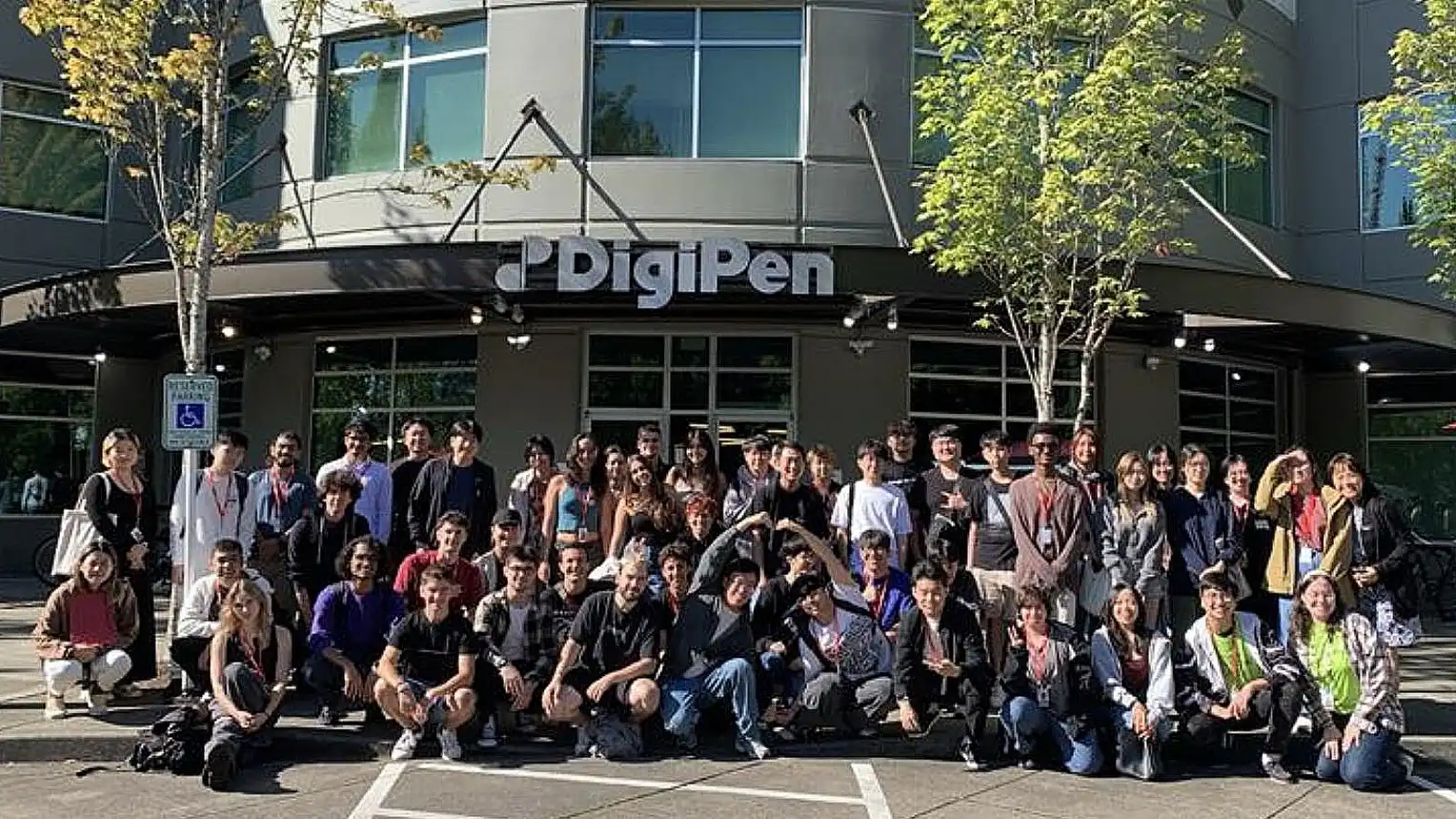 Un gran grupo de alumnado de DigiPen reunido frente al edificio del campus de DigiPen, sonriendo y posando para una foto de grupo.