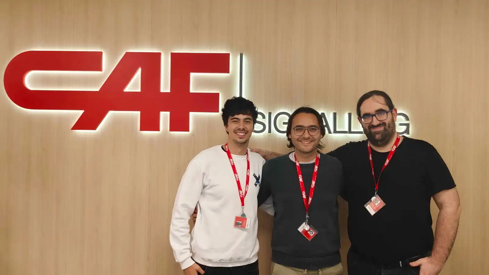 Tres exalumnos de DigiPen posando juntos frente al logo de CAF Signalling, destacando sus logros profesionales en la industria.